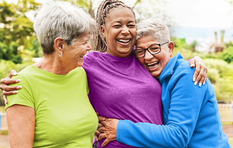 Drei Freundinnen in bunter Kleidung halten sich einander im Arm und sind fröhlich