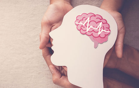 Hände halten ein Kopfumriss mit Gehirn aus Papier