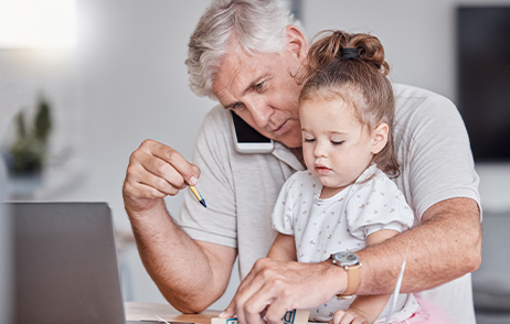 Der Opa telefoniert mit dem Handy und hat dabei seine Enkeltochter auf dem Schoss sitzen