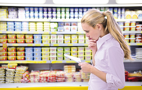 Frau im Supermarkt vor Regal mit kritischem Blick auf Einkaufsliste