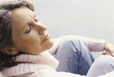 Eine Frau mittleren Alters sitzt bequem und hat die Augen geschlossen.