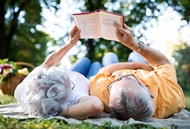Älteres Paar liegt auf einer Decke im Park und liest zusammen ein Buch