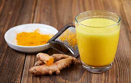 Kurkumawurzel und geriebenes Kurkuma sowie ein Glas Saft mir Kurkuma