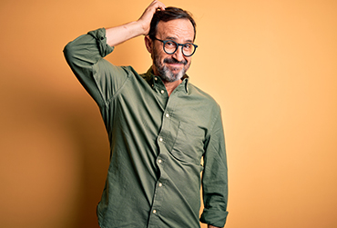 Ein Mann mittleren Alters mit Brille kratzt sich am Kopf und überlegt