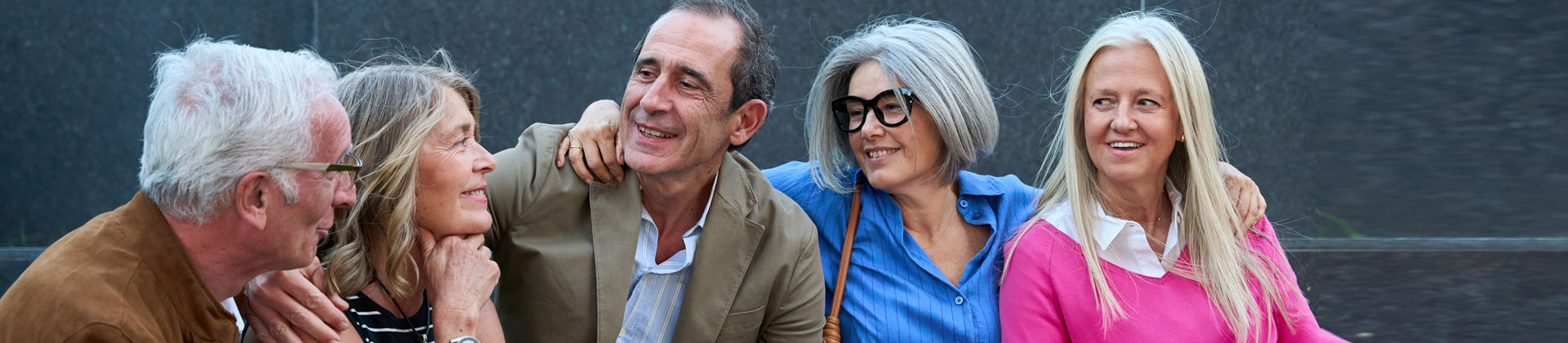 Freunde und Freundinnen im Alter von 50+ sitzen beisammen und erzählen und lachen