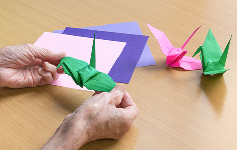 Eine ältere Frau faltet verschiedenfarbige Origami Vögel