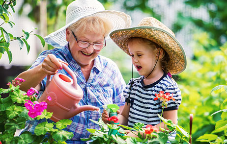 Oma mit Enkel gießen Blumen in einem schönen Garten 