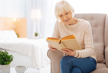 Lesergeschichte aus dem Leben Reife Frau sitzt auf einem gemütlichen Sessel und liest ein Buch