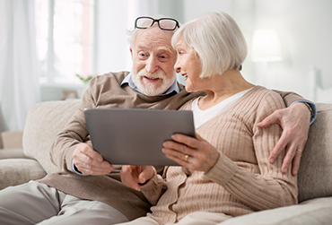 Winter-Unternehmungen fürs Gedächtnis Älteres Paar sitzt auf dem Sofa und hat ein Tablet in der Hand