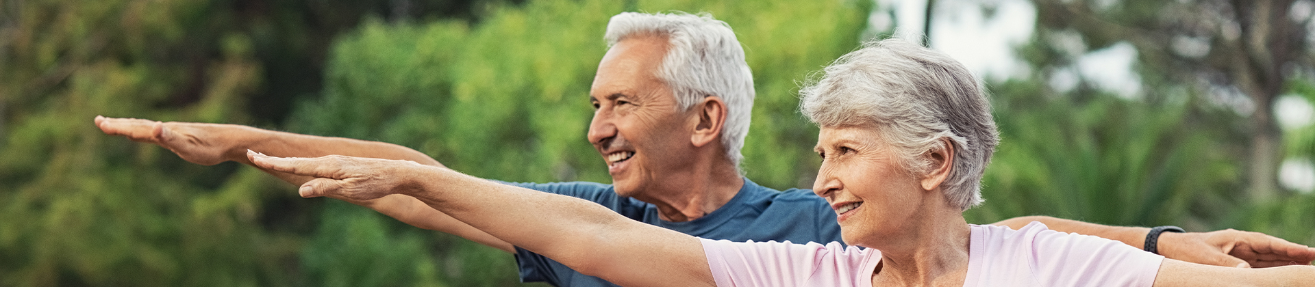 Ein älteres Paar macht im Park Sport und streckt die Arme nach vorne und nach hinten