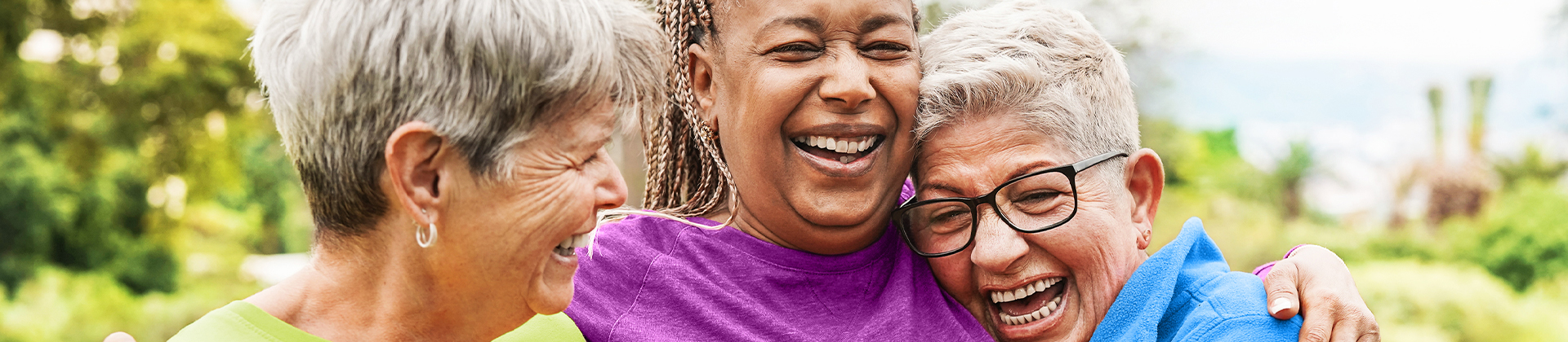 Tag der Freundschaft Drei Freundinnen befinden sich in einem Park. Sie lachen und halten sich im Arm.